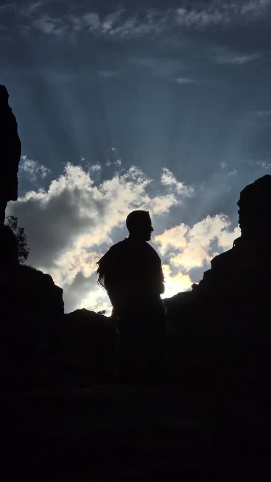 A silhouette on a rock against bright clouds